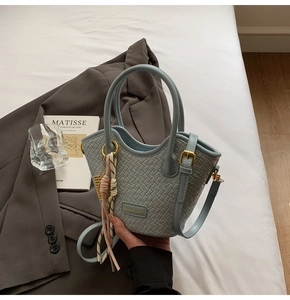 Detail of light blue woven tote bag featuring a pink striped scarf and metal logo plate