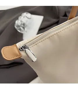 Close-up of smooth silver metal zipper and brown faux leather handle detail on beige tote bag