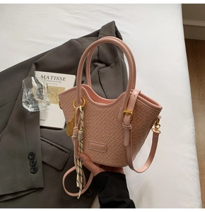 Detail of light pink woven bucket bag with leather brand patch and decorative scarf