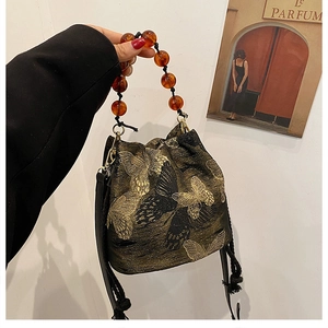 Close-up of black bucket bag with gold butterfly embroidery and amber beaded handle