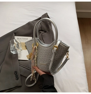 Detail of silver woven bucket bag with circular handles, silk scarf, and metal charms