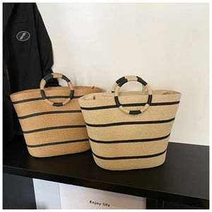 Detail of woven straw tote bag featuring black stripes and round braided handles
