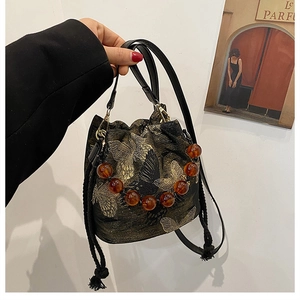 Detail of black drawstring bucket bag with gold butterfly embroidery and amber beaded handle