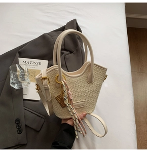 Detail of cream woven handbag with gold hardware and stylish knot charm on gray blazer