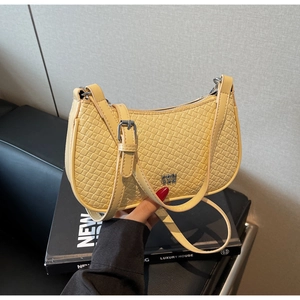 Detail of light yellow crocodile-embossed dumpling bag with silver metal logo and strap