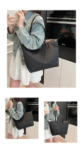 Detail view of large black nylon tote bag with long handles and metal plaque logo
