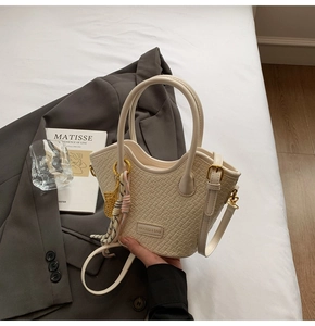 Detail of off-white woven texture handbag with leaf pendant and adjustable strap