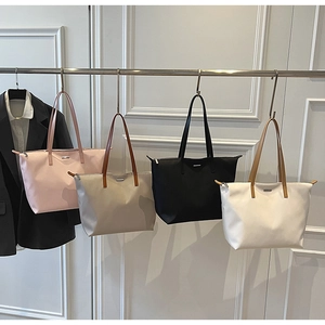Row of large nylon tote bags in pink, taupe, black and white on a metal display rack