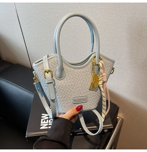Détail du sac seau tressé bleu clair avec plaque logo et breloque raquette de tennis