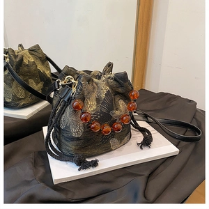 Detail of silk bucket bag featuring golden butterfly embroidery and amber beaded handle