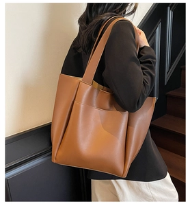 Deep brown matte leather tote bag with exterior pocket shown on shoulder by model
