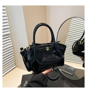 Detail of black glossy leather bucket bag featuring gold hardware and cylindrical handles