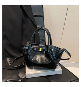 Détail du sac en similicuir noir brillant avec boucle dorée sur fond de veste tailleur