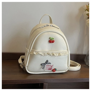 Detail van crème mini-rugzak met kersenbedeltjes, kant en decoratieve strik