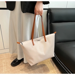 Close-up of beige nylon tote bag with brown leather handles and metal brand tag