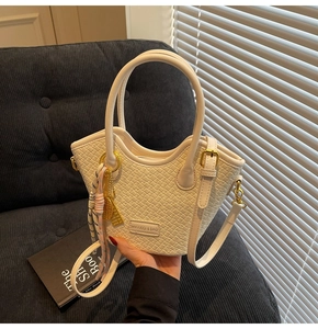 Detailed close-up of cream woven texture hand bag with gold hardware on blue sofa