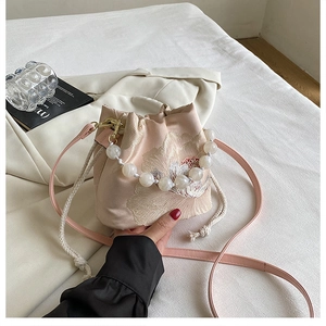Detail of floral embroidery and pearl handle on light pink satin bucket bag