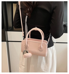 Detail of light pink crossbody bag featuring a heart pendant and adjustable strap