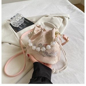Detail of pink embroidered silk bucket bag featuring floral patterns and a pearl handle