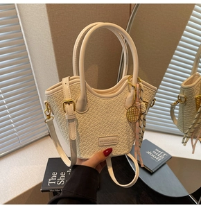 Detail of cream woven bucket bag with metallic logo plate and tennis racket charm