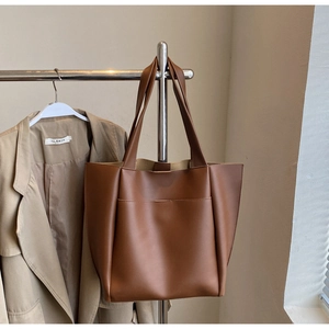 Detailed view of deep brown leather tote bag hanging next to a khaki trench coat