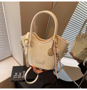 Close-up of cream woven bucket bag with metallic logo and tennis racket charm