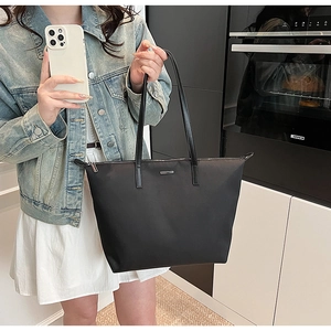Detail of black nylon tote bag with leather strap and silver logo in a modern setting