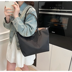 Detail of black tote bag featuring nylon fabric, leather straps and silver zipper