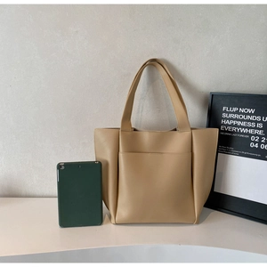 Detail view of large beige tote bag showing open front pocket and wide shoulder straps