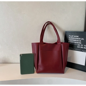 Detail of red leather tote bag with large front pocket showing size against tablet