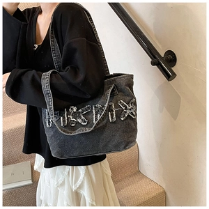 Detail of frayed letter patch on large black washed denim tote bag with vintage edge