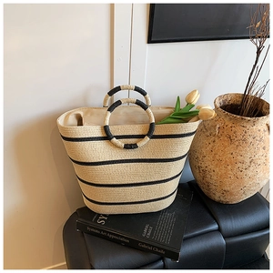 Detail of hand-woven straw tote bag featuring black stripes and round braided handles