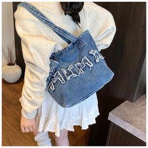 Detail of blue denim tote bag with frayed letter design and crossbody strap on model