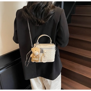 Detail der weißen geflochtenen Box-Tasche mit Plüschbär-Anhänger an einem Model