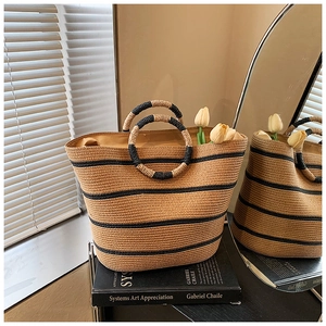 Detail of hand-woven straw tote bag with black stripes and circular handles in sunlight