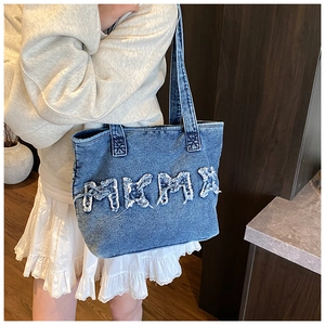 Detailed view of dark blue denim tote bag featuring white frayed letter patchwork accents