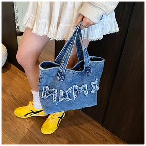 Detail of blue denim tote bag with frayed BMMX letter patches and casual styling
