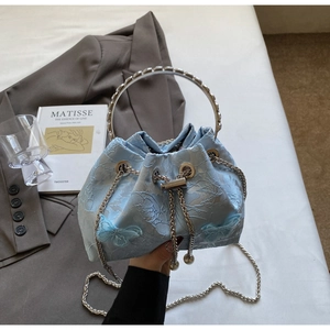 Detail of light blue bucket bag with jacquard fabric, floral accents, and silver chain strap