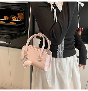 Detailed view of pink leather handbag with heart pendant shown in a lifestyle scene