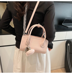 Detail of pink faux leather crossbody bag with heart pendant shown in a lifestyle setting