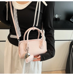 Detail of pink crossbody handbag featuring round handles and heart-shaped charm accessory
