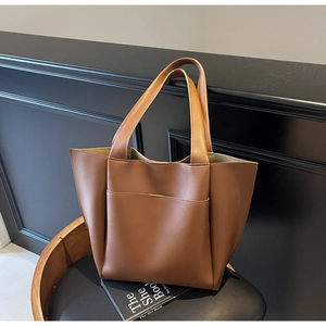 Minimalist brown leather tote bag with front pocket detail on a stylish vintage chair