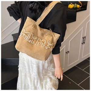 Detail of frayed letter patch on yellow washed canvas tote bag with retro streetwear style