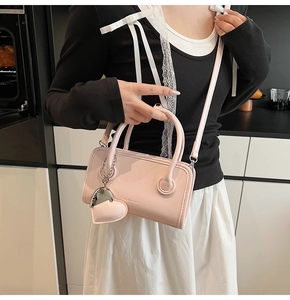 Detail of light pink faux leather handbag with embossed logo and heart pendant