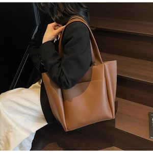 Detail of a large brown leather tote bag held by a model on wooden stairs