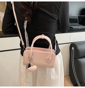 Detail of pink faux leather crossbody bag featuring a heart-shaped charm and logo