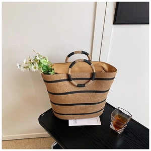 Detail of hand-woven straw beach bag featuring round handles and black stripe accents