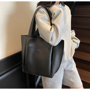 Minimalist black tote bag with large front pocket and matte leather texture on a model