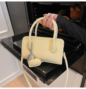 Close-up of cream yellow leather handbag with heart charm and clear embossed logo