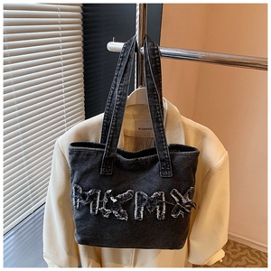 Close-up of black washed denim tote bag with frayed 3D letter patchwork and straps